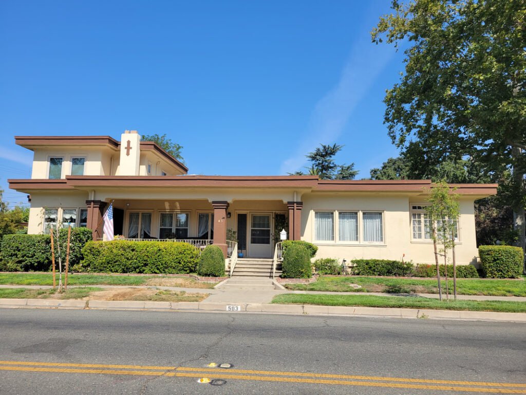 2 Story house, bushes in front, nice porch, beige and maroon colored